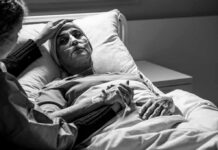 Grandma’s Death Sparks Criminal MAiD Investigation Patient in hospital bed with nasal oxygen held by visitor