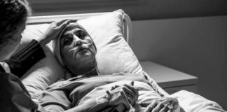 Patient in hospital bed with nasal oxygen held by visitor