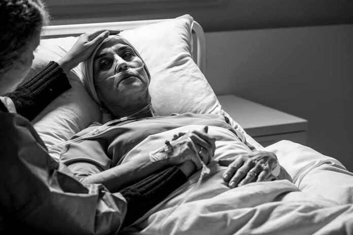 shutterstock_1677368530 Patient in hospital bed with nasal oxygen held by visitor