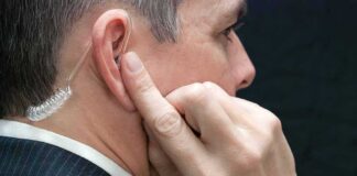 Man wearing clear earpiece touching his ear