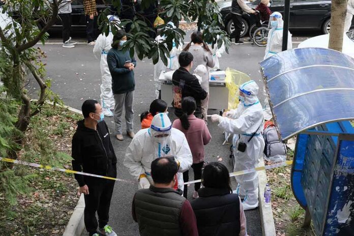 shutterstock_2140295957 Christian Jones and others wait at an outdoor COVID-19 testing site with staff in protective suits
