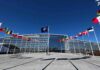 NATO headquarters with member flags in front under a clear blue sky