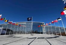 NATO headquarters with member flags in front under a clear blue sky
