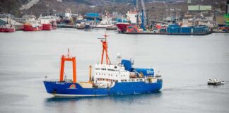 Blue research vessel in harbor with orange cranes