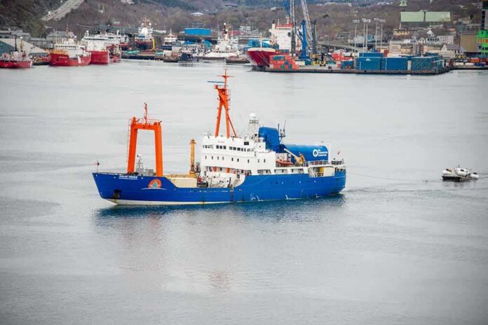 shutterstock_2320246961 Blue research vessel in harbor with orange cranes