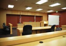 Police Boss Nabbed – Chilling Allegations Emerge Interior view of an empty courtroom with wooden furniture and American flags