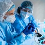 Scientists in protective gear working with a syringe in a laboratory