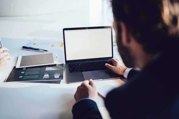shutterstock_1797490516 Person working at a laptop with blank screen on a desk