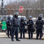British Base Scare – Tehran Named Group of police officers in riot gear standing on a street; Brian Folkerts present
