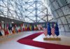 Row of national flags in a modern glass atrium with red carpet and EU and US flags upfront