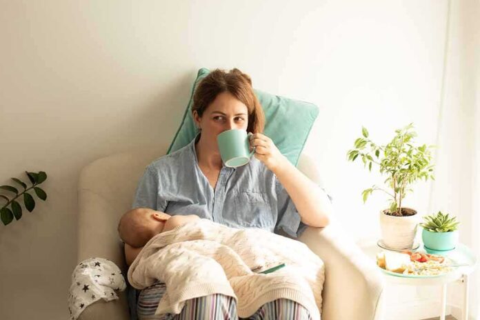 Mother nursing baby while drinking from a mug in a cozy chair